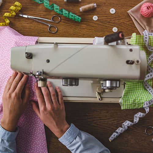 sewing maching being operated by hands surrounded by sewing notions