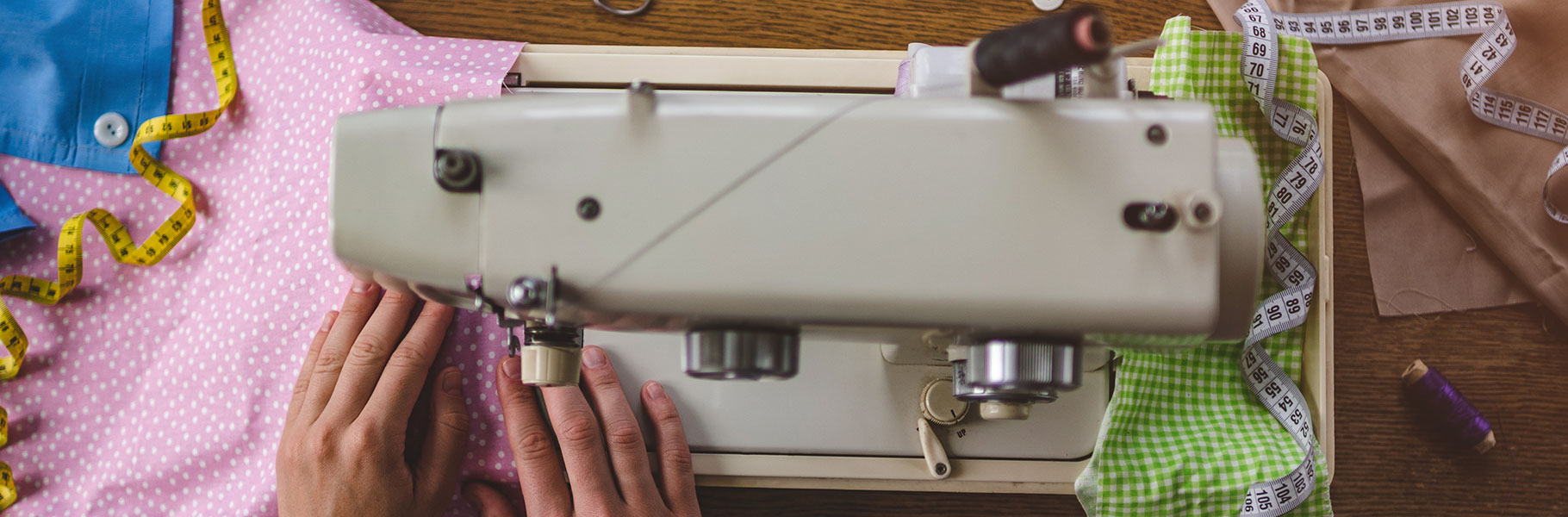 hands working sewing machine surrounded by sewing notions