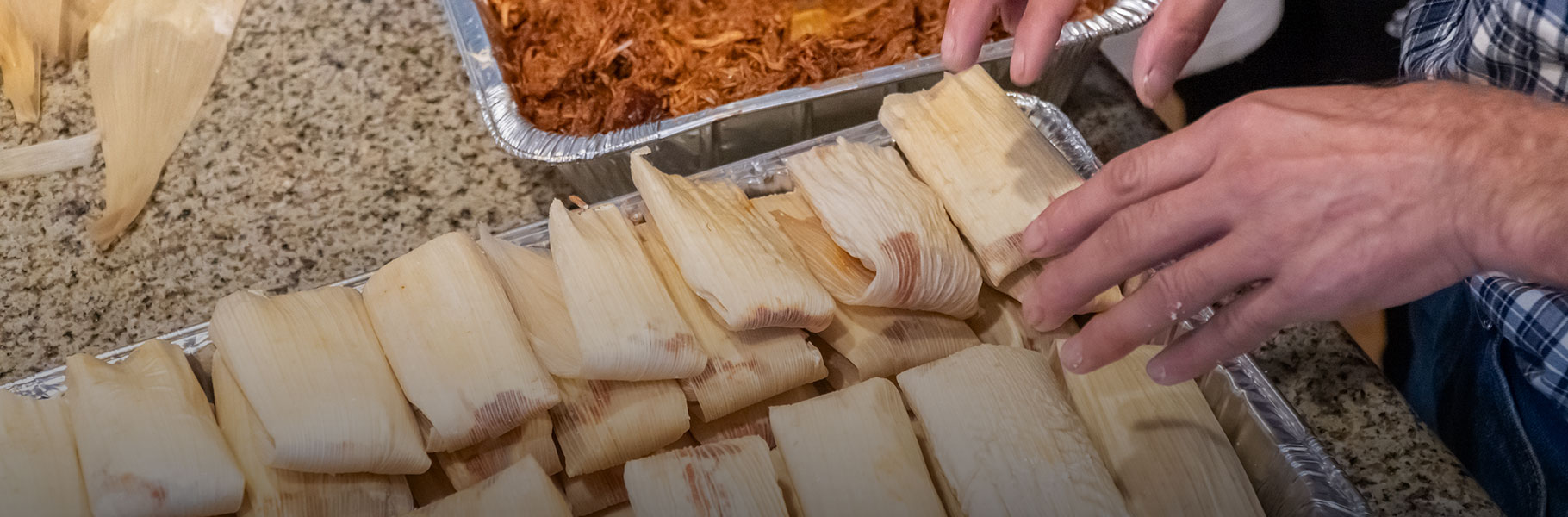 hands assembling a casserole dish full of tamales