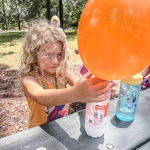 Elementary aged student working on science project with balloons outdoors during Rebel Quest