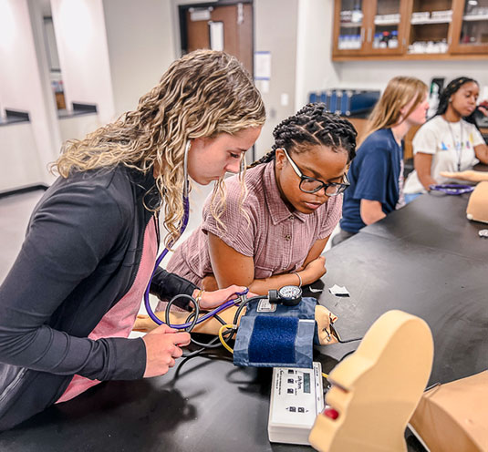 Two students looking at blood pressure cuff in Rebel pharmacy program